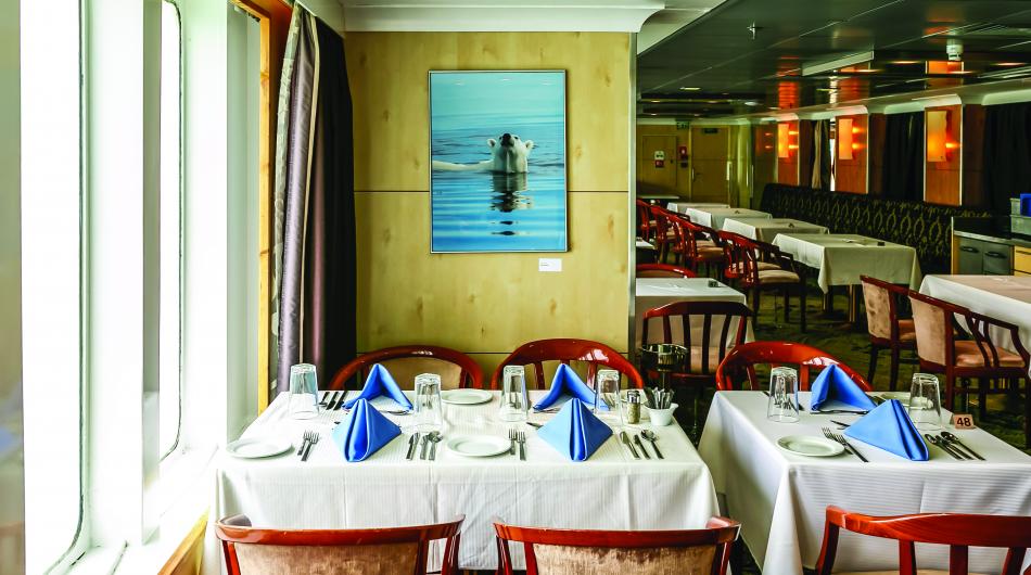 Dining tables are set with white tablecloths and cutlery on the Ocean Endeavour