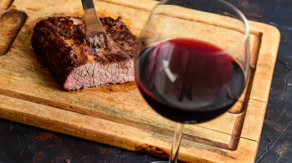 Glass of wine with steak on a rectangular wooden cutting plate