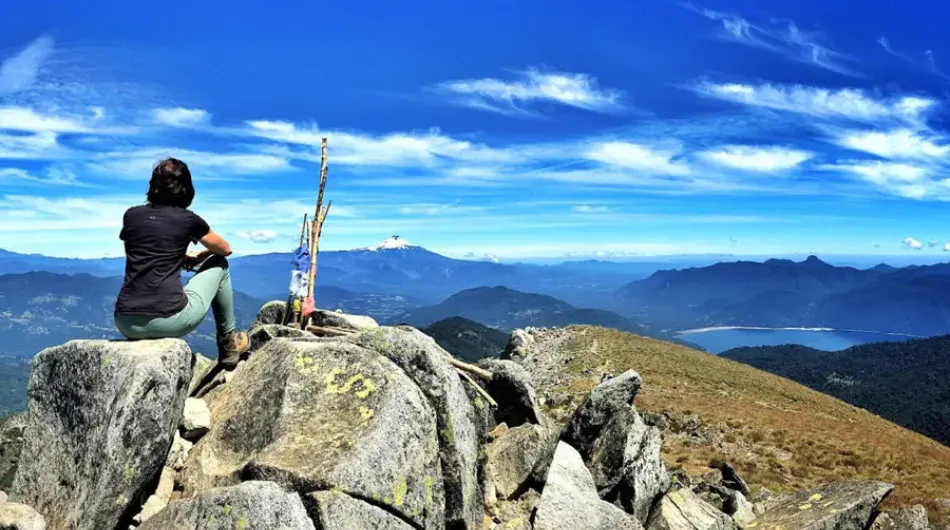 Trekker sitting on top of rocky mountain top overlooking landscape
