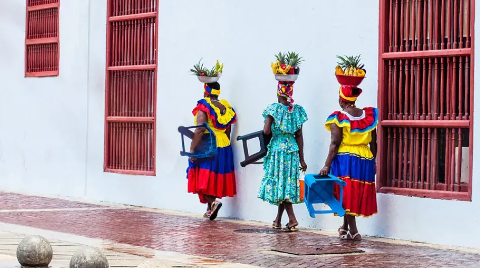 Three colorful colombian ladies carying fruit basket on their heads
