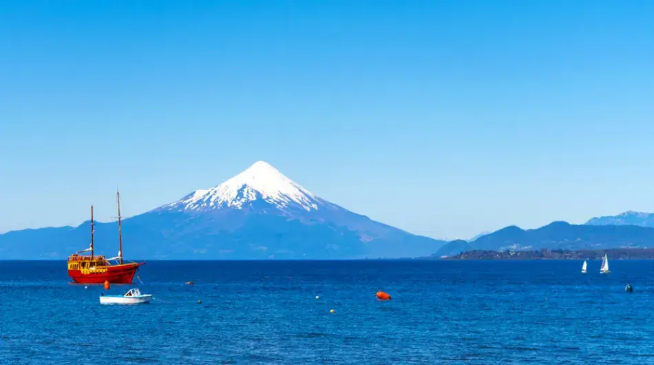 Llanquihue lake with red ship and snowy osorno volcano