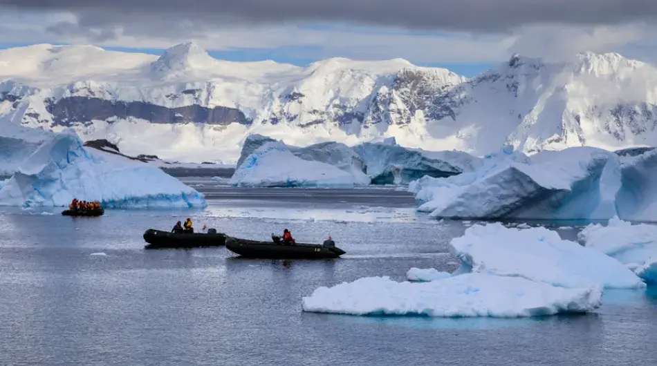 Zodiacs cruising through icy waters with icebergs with snowy Antarctic mountains