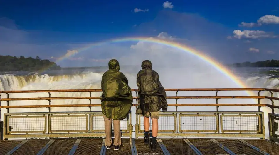 Couple standing in front of iguazu falls with a rainbow over their heads