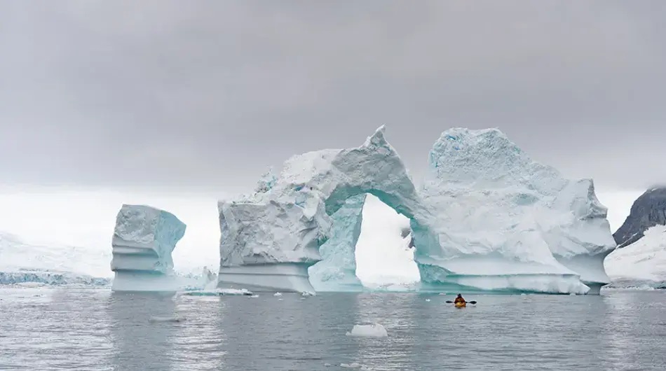 kayaker near iceberg arch in Antarctica 