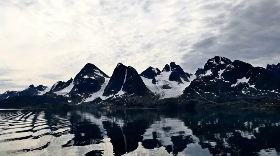 Kangerlussuatsiaq Fjord in Greenland with very calm water with steep snow covered mountains in reflection