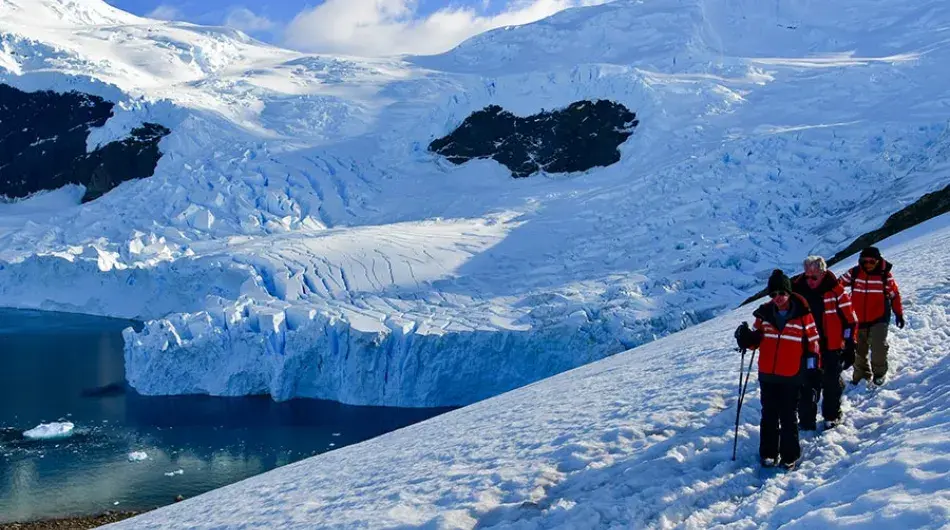 Tourists hiking in snow on hillside in Antarctica with bay and mountains in background