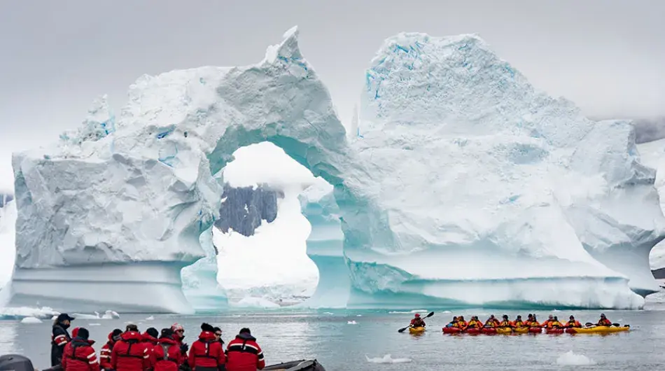 Tourists in zodiac cruising past giant arch iceberg in Antarctica