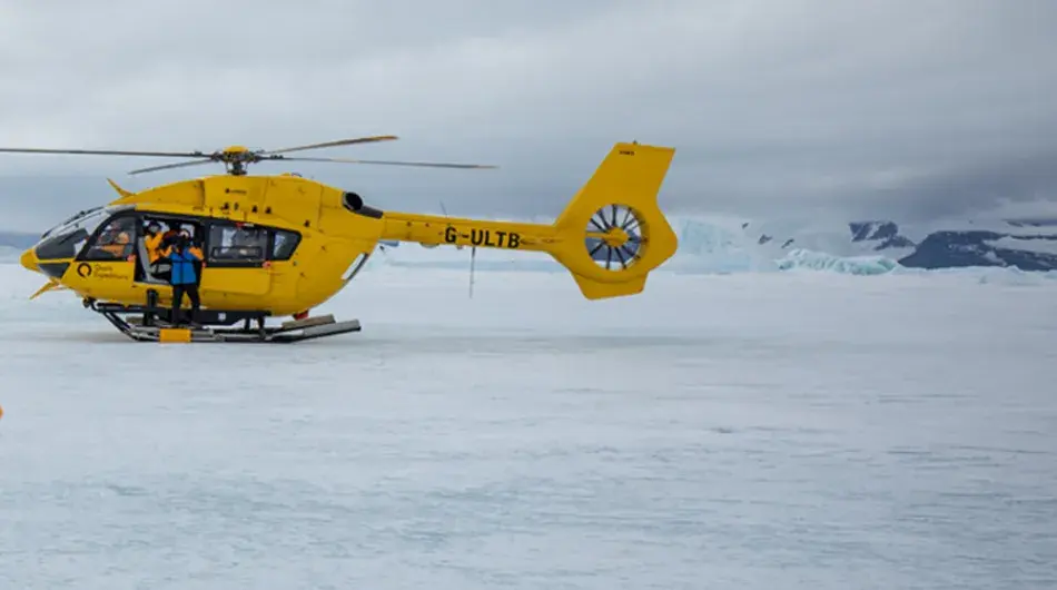 Quark yellow helicopter landing on ice shelf in Antarctica with photo by Michelle Sole