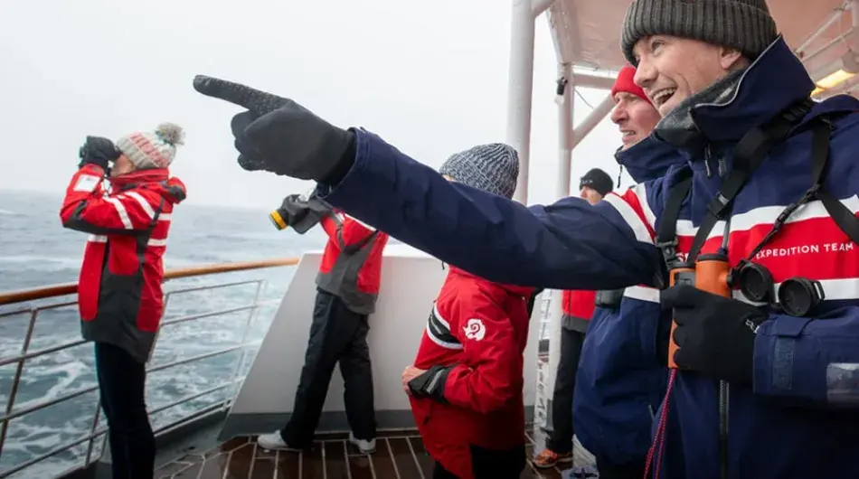 Expedition crew pointing out wildlife sighting to tourists in Antarctica