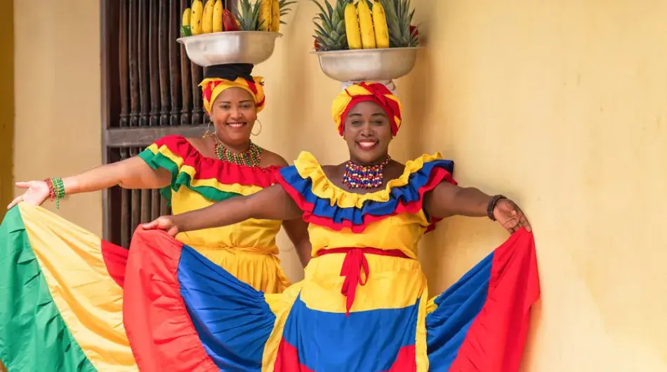 Two Colombian ladies in colourful dresses with fruit baskets on their heads