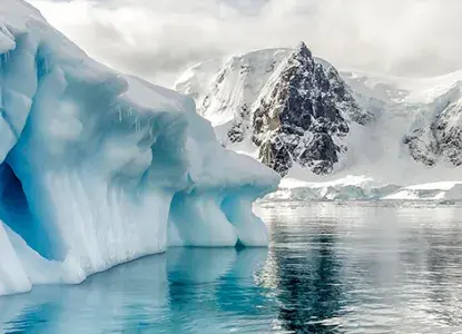 interesting blue iceberg formation in calm Antarctic waters in Polar Circle with snowy mountains in background) 